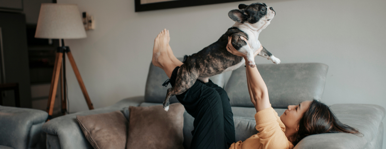 A woman lifts her dog in the air while sitting on the couch.