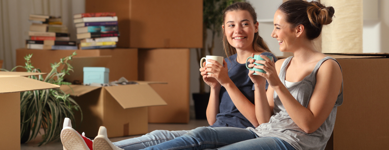 Two young women co-buying a home sit in their new house surrounded by boxes.