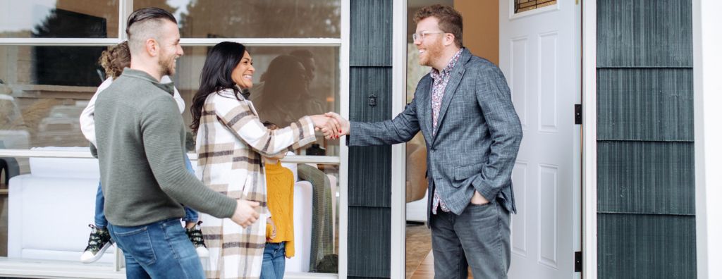 A heterosexual interracial family shake hands with their real estate agent on the front porch as they accept a contingent offer for their home.