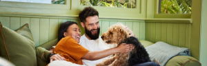 Laughing young couple petting their dog while sitting together on a sofa in their living room at home