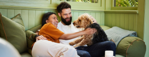 Laughing young couple petting their dog while sitting together on a sofa in their living room at home